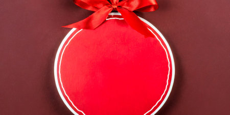 Red gift box with a red bow on a dark red background.の素材