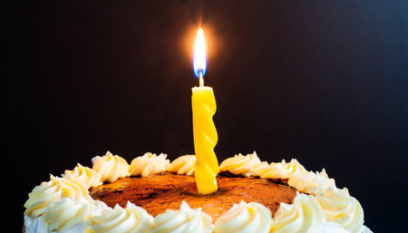 Birthday cake with burning candle on black background, close-upの素材
