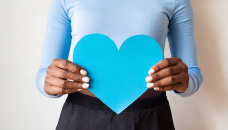 Close-up of woman holding blue paper heart against white background.の素材