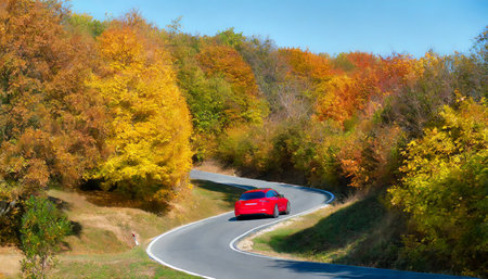 Autumn landscape with a red car on the road in the mountainsの素材