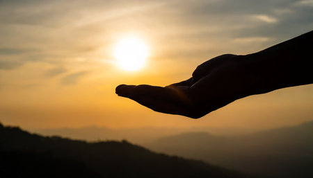 Silhouette of hand holding the sunset on the mountain background.の素材