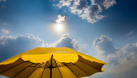 Yellow beach umbrella on blue sky with sun light. Summer vacation conceptの素材