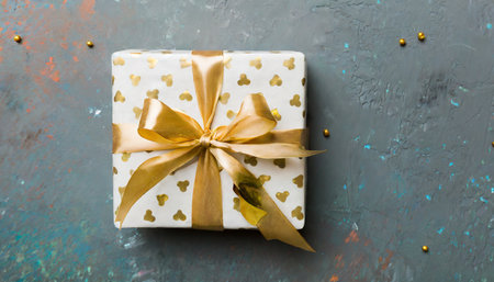 wrapped christmas or other holiday handmade present in white paper with gold ribbon on colored background present box decoration of gift on colored table top view with copy spaceの素材