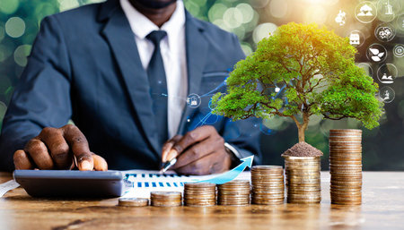 businessman using a calculator and tree growing on money coin stack with growth graph concept of green business growth or green investment finance and sustainability investment carbon creditの素材