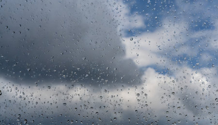 window raindrops on surface against blue cloudy sky after storm rainy weatherの素材
