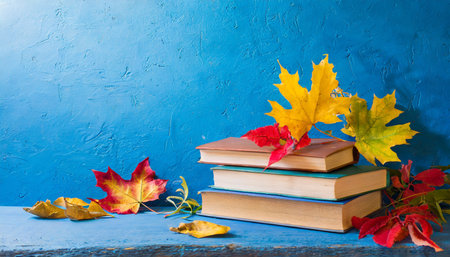 Books and autumn leaves on blue background. Back to school. Copy space.の素材