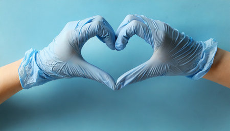 hand in medical gloves in shape of heart on blue backgroundの素材