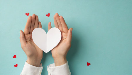 first person top view photo of valentine s day decorations girl s hands in white stylish shirt holding white paper heart on pastel blue background with blank spaceの素材