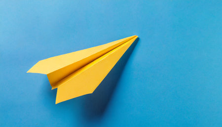 top view of yellow paper airplane on blue background with customizable space for textの素材