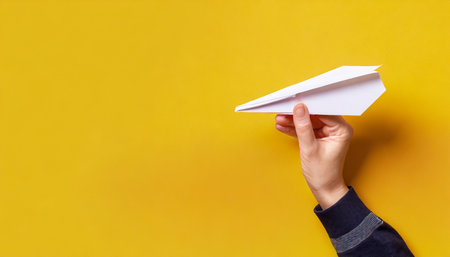 hand holding paper plane over yellow background panoramic mock up imageの素材