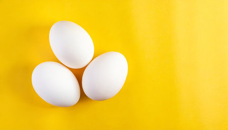 three white eggs on a yellow background top viewの素材