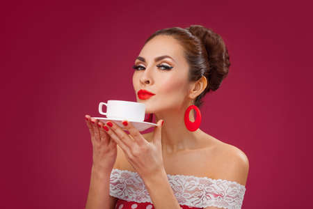 Funny portrait of cute young female model with cup in her arms wearing red dressの写真素材