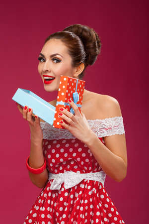 Funny portrait of a smiling cute young female model opening gift box in wearing red dressの写真素材