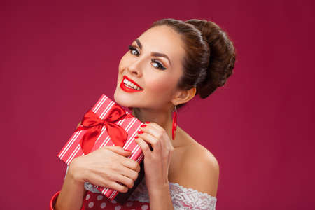 Funny portrait of a smiling cute young female model embraces gift box. Pink Backgroundの写真素材