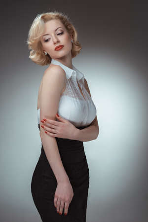 Pin-up girl, 50 style. Studio shot of young and beautiful woman wearing white blouse and black fitting, in studio. Professional makeup and hair styleの写真素材