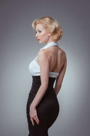 Pin-up girl, 50 style. Studio shot of young and beautiful woman wearing white blouse and black fitting, in studio. Professional makeup and hair styleの写真素材