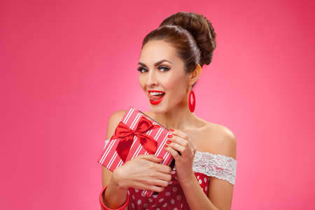 Funny portrait of a smiling cute young female model embraces gift box. Pink Backgroundの写真素材