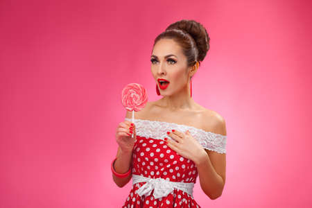 Funny portrait of cute young female model with candy in her arms wearing red dressの写真素材