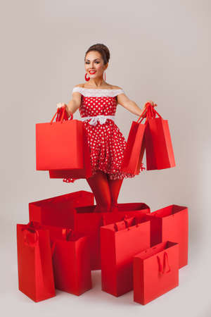 Funny portrait of a smiling cute young female model holding many shopping bags in her arms wearing red dressの写真素材