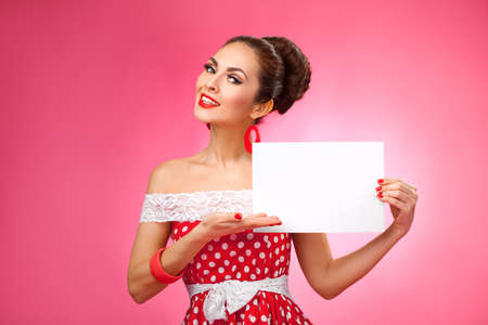 Portrait of a smiling cute young female model with blank sign in her arms wearing red dressの写真素材