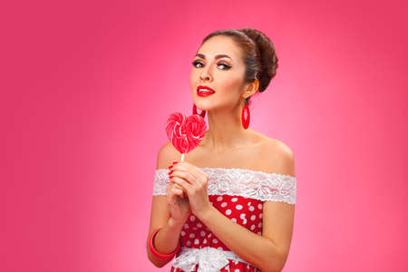 Funny portrait of cute young female model with candy in her arms wearing red dressの写真素材