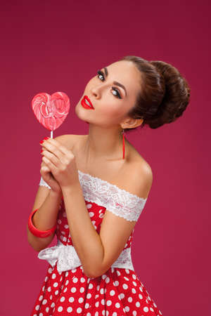 Funny portrait of cute young female model with candy in her arms wearing red dressの写真素材