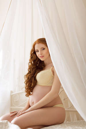 Slim beautiful pregnant woman sitting on the bed in the bedroom. Beautiful lingerie. Stylish and sexy pregnancy.の写真素材