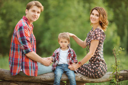 Happy Family on the nature. Mother father and son in casual clothes, sit on a fence, rural look , outdoorsの写真素材