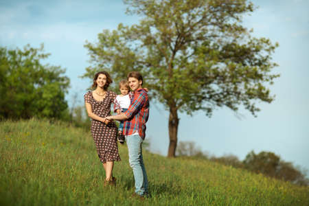 Photo of a young family enjoying a stroll in the park on a sunny summer day. Big family tree on the backgroundの写真素材