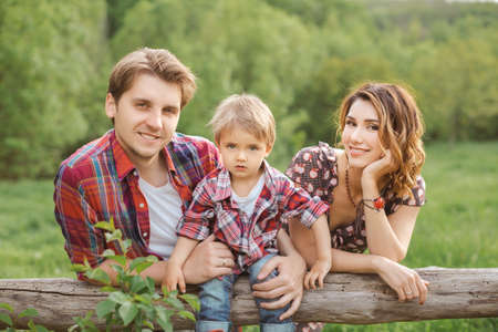 Happy Family on the nature. Mother father and son in casual clothes, sit on a fence, rural look , outdoorsの写真素材