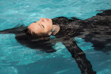 Portrait of the beautiful woman in black dress floating in blue waterの写真素材
