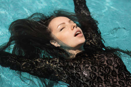 Portrait of the beautiful woman in black dress floating in blue waterの写真素材