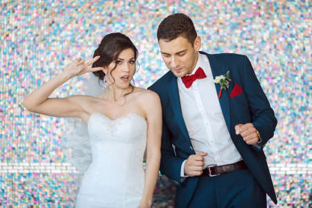 Wedding couple in love. Beautiful bride in white dress and veil with handsome groom in blue suite dancing and having fun indoors against beautiful colored background bokeh like their good mood. Close-up portrait of man and girl in fanny posesの写真素材