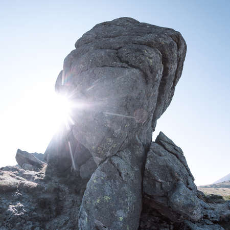 View of the high mountains with big rock on the foreground. Rays of the sun. Square shotの写真素材