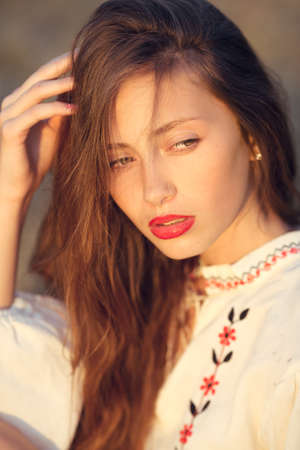 Slav teen girl portrait. Happy woman sitting on yellow meadow in national ukrainian clothing.の写真素材