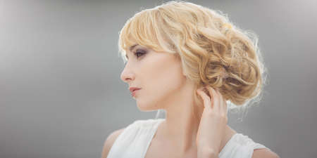 Portrait of a young beautiful bride looking down gently touching her hair outdoors on gray...