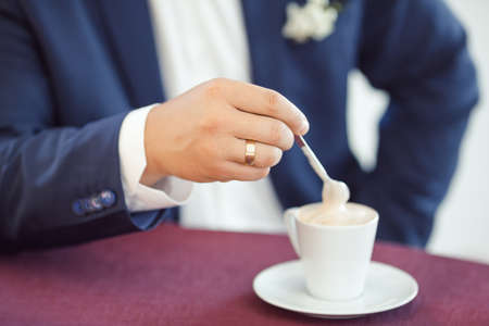 Groom's hands whith gold ring holding spoon in cup of coffeeの写真素材