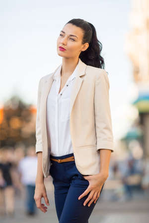 Beautiful brunette business woman in pink suit standing outdoors against gray city space background and looking away. Copy spaceの写真素材