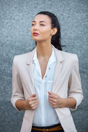 Beautiful brunette business woman in suit standing outdoors against gray background and looking away. Copy spaceの写真素材