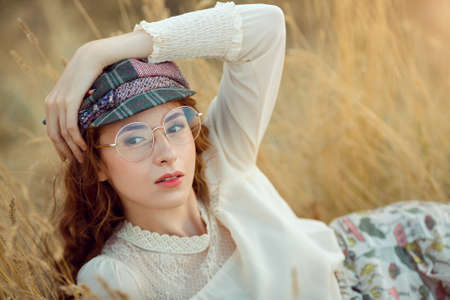 Woman writer concept. Student thinking and looking at camera lying on yellow grass outdoors. Joyful happy girl student with pencil outside on the nature. Retro look.の写真素材