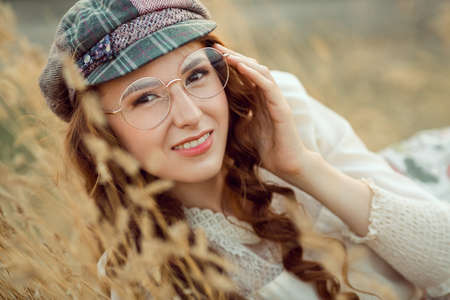 Woman writer concept. Student thinking and looking at camera lying on yellow grass outdoors. Joyful happy girl student with pencil outside on the nature. Retro look.の写真素材