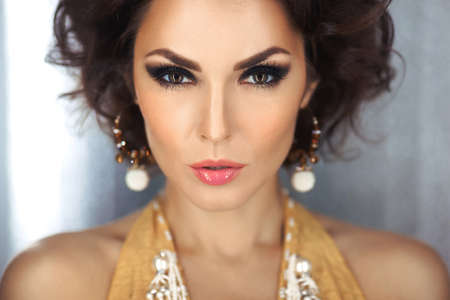 Beautiful woman with evening make-up and curly hair and yellow dress with jewelry pearls. Smoky...