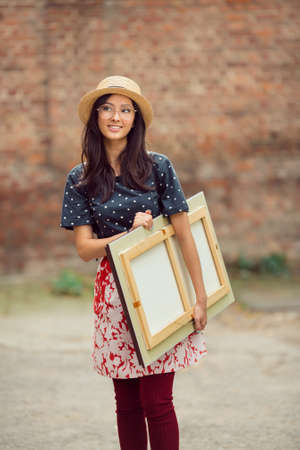 Young Asian woman with painting outdoors. Mixed race student girl on university college campus park...