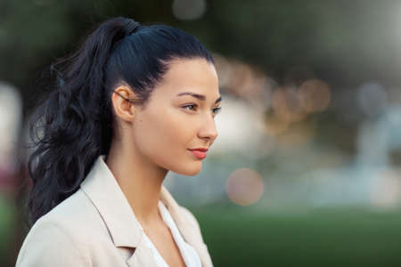 Woman smiling - side view portrait of happy lovely and beautiful mixed race asian caucasian young businesswoman in casual clothes outdoor in the city parkの写真素材