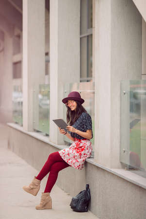Woman using tablet outdoors in city. Young girl sitting with tablet pc and backpack.の写真素材