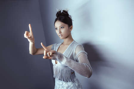 New technology and communication concept -modern woman of the future working with imaginary virtual screen. Fashion futuristic young attractive multi-racial Asian Caucasian model portrait with futuristic make-up indoors. Copy space for your text.の写真素材