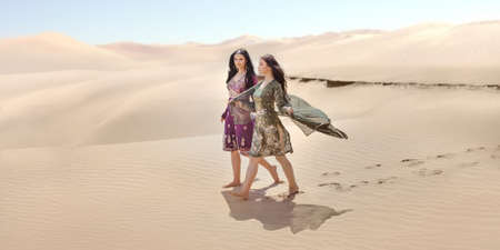 Travel concept. Adventure of two sisters princesses happy standing in the desert and looking at landscape. Two beautiful mixed race asian caucasianl girls enjoy a joint journey. Creative art fashion shot of two gorgeous attractive models outdoors in arabiの写真素材