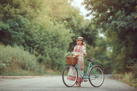 Pregnant girl retro French style with bicycle on a forest road. Beautiful pregnancy concept. Blonde happy woman with curly hair on nature background.の写真素材