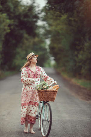 Pregnant girl retro French style with bicycle on a forest road. Beautiful pregnancy concept. Blonde happy woman with curly hair on nature background.の写真素材
