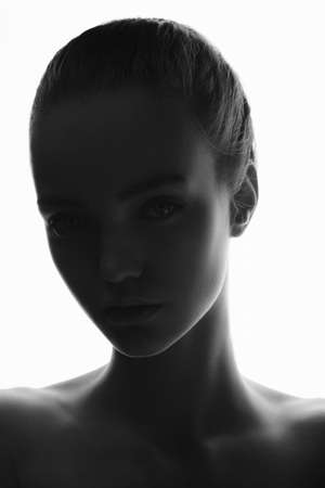 Mysterious silhouette portrait of young teen girl in studio on a white background. Creative fashion model shot with perfect skin. Black and White photoの写真素材